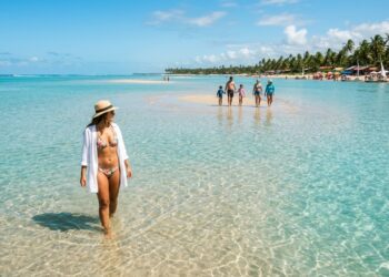 A praia nordestina com águas cristalinas como vidro e um mar que recua revelando bancos de areia