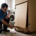 Marceneiro examinando a base estufada de um armário de MDF e a porta desalinhada no piso de uma lavanderia
