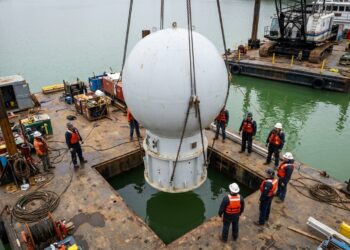 Guindaste içando a esfera oca branca Dongchu-1 sobre uma balsa antes de mergulhá-la na água do lago.