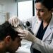 Médico dermatologista examinando a raiz do cabelo e o couro cabeludo de um paciente com dermatoscópio em consultório clínico