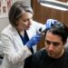 Médico dermatologista examinando minuciosamente o couro cabeludo de um paciente sob iluminação clínica direcionada