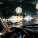 Visão do motorista através do para-brisa à noite com faróis de veículos formando halos luminosos e ofuscamento na pista molhada.