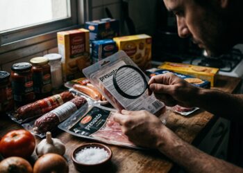 Consumidor examinando a tabela nutricional de um produto alimentício industrializado em uma bancada de cozinha