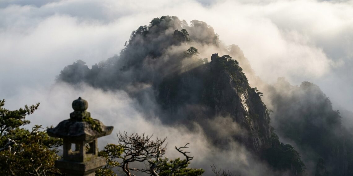 Pico de montanha japonesa firme e imponente cercado por densa neblina matinal sob a luz do amanhecer.
