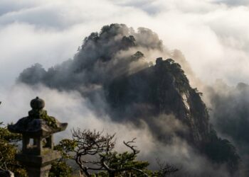 Pico de montanha japonesa firme e imponente cercado por densa neblina matinal sob a luz do amanhecer.
