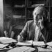 Albert Einstein sentado em seu escritório histórico cercado por papéis manuscritos e luz natural entrando pela janela