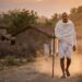 Mahatma Gandhi caminhando com cajado de madeira por estrada de terra na Índia em luz suave do entardecer