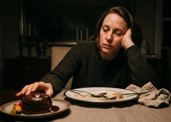 Pessoa com expressão de cansaço segurando a cabeça após o almoço diante de uma mesa de refeição