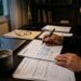 Pessoa revisando documentos financeiros e calendário em mesa de casa, xícara de café ao lado, sugerindo pausa antes de decidir