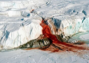 Cachoeira de água vermelho-ferrugem desaguando entre fendas e paredões de gelo branco em uma geleira na Antártida.