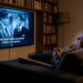 Pessoa descansando no sofá da sala escura enquanto assiste a filme na televisão com legendas ativadas