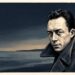 Ilustração editorial de Albert Camus com sobretudo de gola levantada e olhar reflexivo sobre fundo em tons de azul-marinho