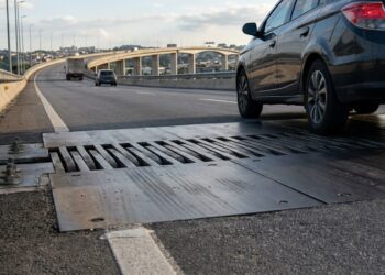 Rodas de um carro passam sobre uma junta de dilatação instalada transversalmente na pista de uma ponte.