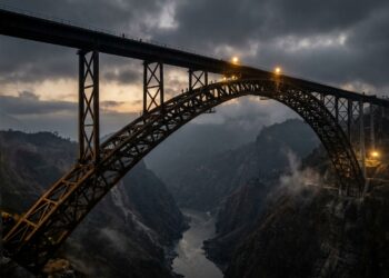 Vista aérea lateral da Chenab Rail Bridge destacando seu grande arco metálico e o tabuleiro ferroviário sobre o desfiladeiro nos Himalaias