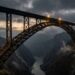 Vista aérea lateral da Chenab Rail Bridge destacando seu grande arco metálico e o tabuleiro ferroviário sobre o desfiladeiro nos Himalaias
