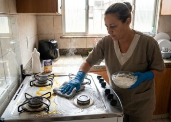 Faxineira aplica detergente com bicarbonato sobre gordura no fogão.