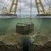 Corte submarino mostra estrutura de concreto sendo baixada até o leito marinho.