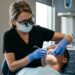 Periodontista com lupa cirúrgica e luvas examinando a mordida e a estabilidade dental de paciente na cadeira odontológica.