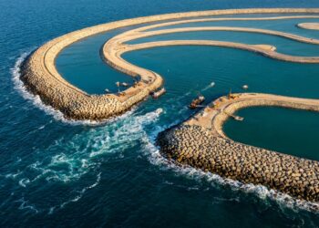 Vista aérea do quebra-mar curvado de Palm Jumeirah mostrando uma das aberturas artificiais por onde a água do mar aberto circula em direção aos canais internos.