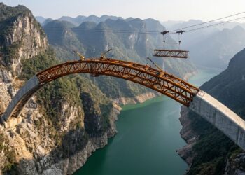 Arco de 600 metros da Ponte Tian’e Longtan atravessa um desfiladeiro na China com sua estrutura tubular de aço parcialmente exposta.