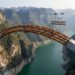 Arco de 600 metros da Ponte Tian’e Longtan atravessa um desfiladeiro na China com sua estrutura tubular de aço parcialmente exposta.