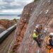 Encosta sobre ferrovia britânica coberta por redes metálicas e grandes ancoragens instaladas na rocha.