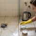 Pessoa prepara bicarbonato e sal ao lado de um ralo de banheiro com água acumulada.
