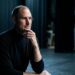 Steve Jobs de perfil reflexivo em palco escuro com iluminação pontual suave