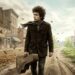 Bob Dylan caminha por uma estrada enquanto a paisagem ao redor representa a passagem do tempo e a mudança.