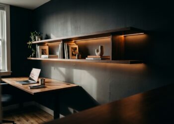 Prateleira suspensa minimalista com LED integrado flutuando na parede de home office compacto, com mesa de trabalho vazia abaixo e luz natural misturada com iluminação de fita LED