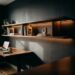Prateleira suspensa minimalista com LED integrado flutuando na parede de home office compacto, com mesa de trabalho vazia abaixo e luz natural misturada com iluminação de fita LED