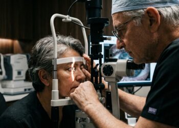 Médico oftalmologista experiente examinando olho de paciente na lâmpada de fenda em consultório clínico.