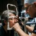 Médico oftalmologista experiente examinando olho de paciente na lâmpada de fenda em consultório clínico.