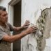 Pintor profissional inspecionando parede com tinta descascando e manchas escuras de mofo no reboco