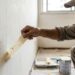 Pintor retira fita adesiva da parede para verificar se a tinta antiga está solta.