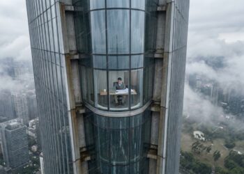Pessoa trabalha no último andar de um arranha-céu enquanto a estrutura se movimenta levemente sob a ação do vento.