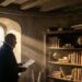 Michel de Montaigne observando a paisagem através da janela de pedra em sua biblioteca renascentista de carvalho.