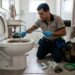 Encanador inspeciona vaso sanitário entupido ao lado de itens como lenços umedecidos, fio dental, cabelo e hastes flexíveis.