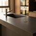 Cuba esculpida em quartzo sintético integrada continuamente na bancada de cozinha moderna, com superfície monolítica e refletiva destacando a resistência do material