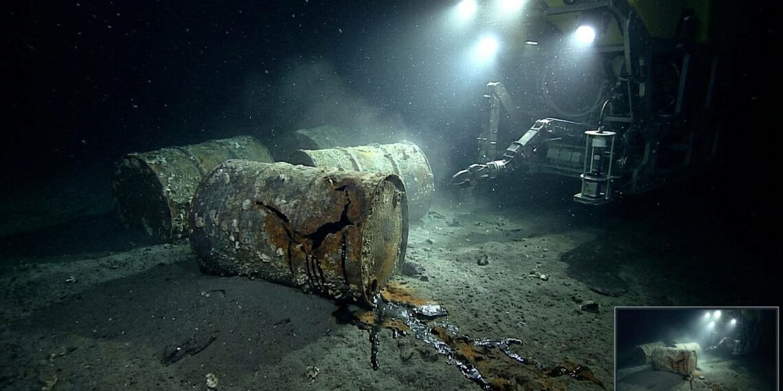 Barris de lixo nuclear oxidados e rompidos repousando no sedimento do leito marinho abissal a quase 5 mil metros de profundidade sob a luz de submersível
