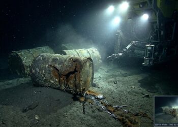Barris de lixo nuclear oxidados e rompidos repousando no sedimento do leito marinho abissal a quase 5 mil metros de profundidade sob a luz de submersível