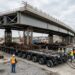 Carretas modulares com dezenas de eixos transportam uma ponte de 3.500 toneladas até seus pilares.