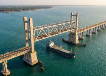 Vão ferroviário da Nova Ponte Pamban elevado entre duas torres enquanto uma embarcação passa pelo canal abaixo.