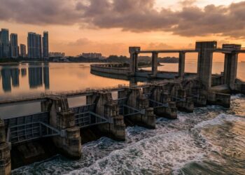 Vista aérea da barreira de 350 metros e nove comportas da Marina Barrage represando o reservatório com arranha-céus de Singapura ao fundo.
