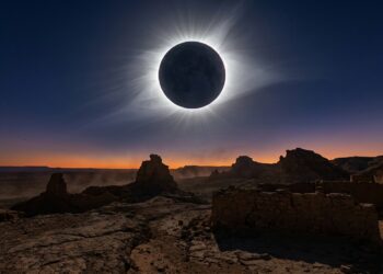 Silhueta ampliada da Lua cobrindo totalmente o disco do Sol e projetando a coroa solar prateada sobre horizonte desértico