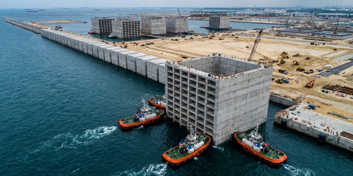 Caixão gigante de concreto é transportado pelo mar para formar o paredão do Tuas Port.