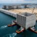 Caixão gigante de concreto é transportado pelo mar para formar o paredão do Tuas Port.