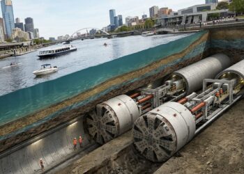 Duas tuneladoras gigantes avançam sob o rio Yarra enquanto barcos navegam na superfície.