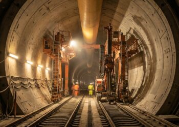 Interior de túnel ferroviário circular em construção sob os Alpes com aduelas de concreto e trilhos sob holofotes