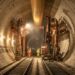 Interior de túnel ferroviário circular em construção sob os Alpes com aduelas de concreto e trilhos sob holofotes